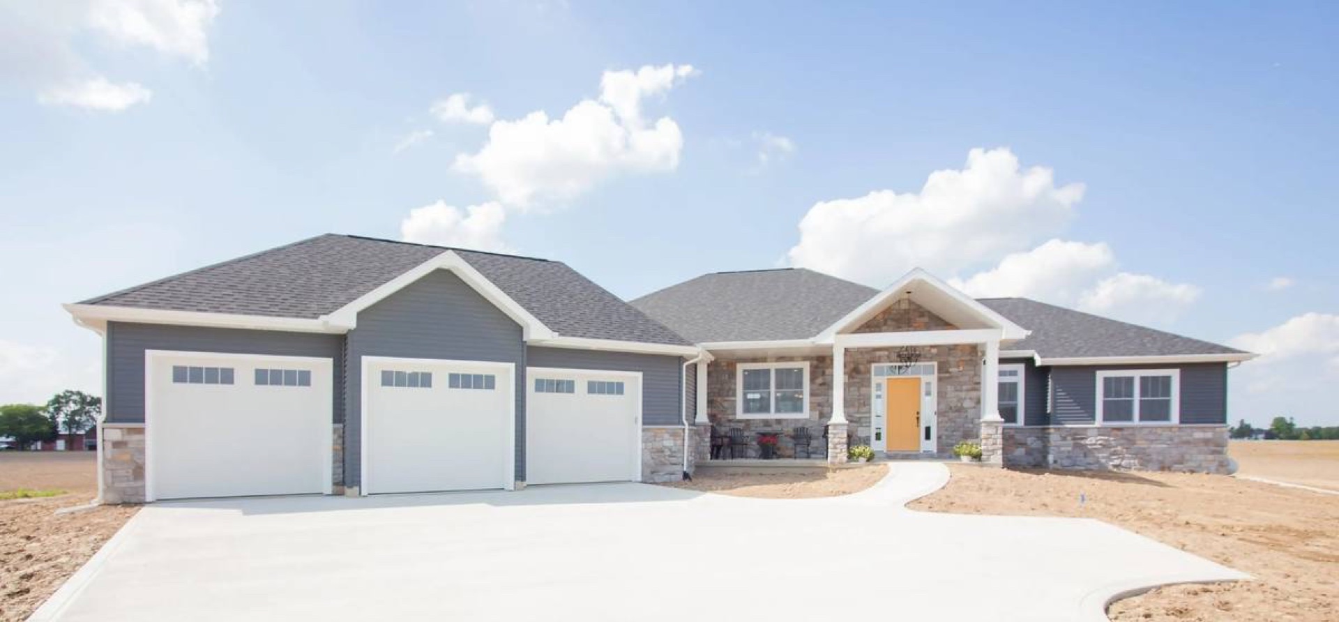 Custom ranch home with three-car garage, stone facade, and tan front door