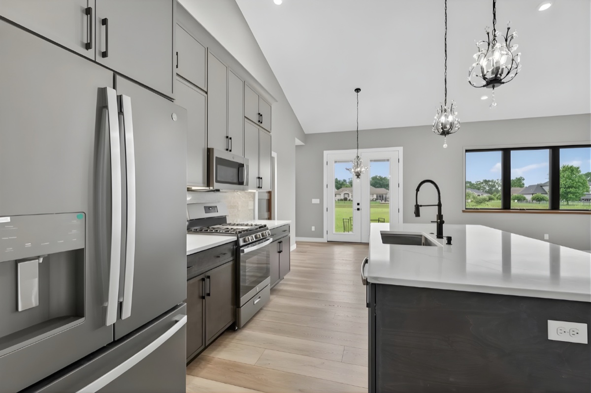 Custom kitchen with vaulted ceiling, crystal chandeliers, gray cabinetry, and dark island