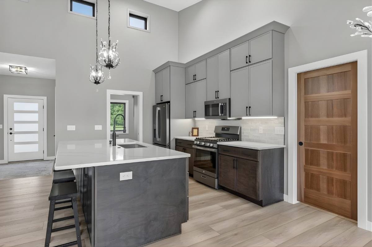 Custom kitchen with tall gray shaker cabinets, dark island base, and stainless appliances
