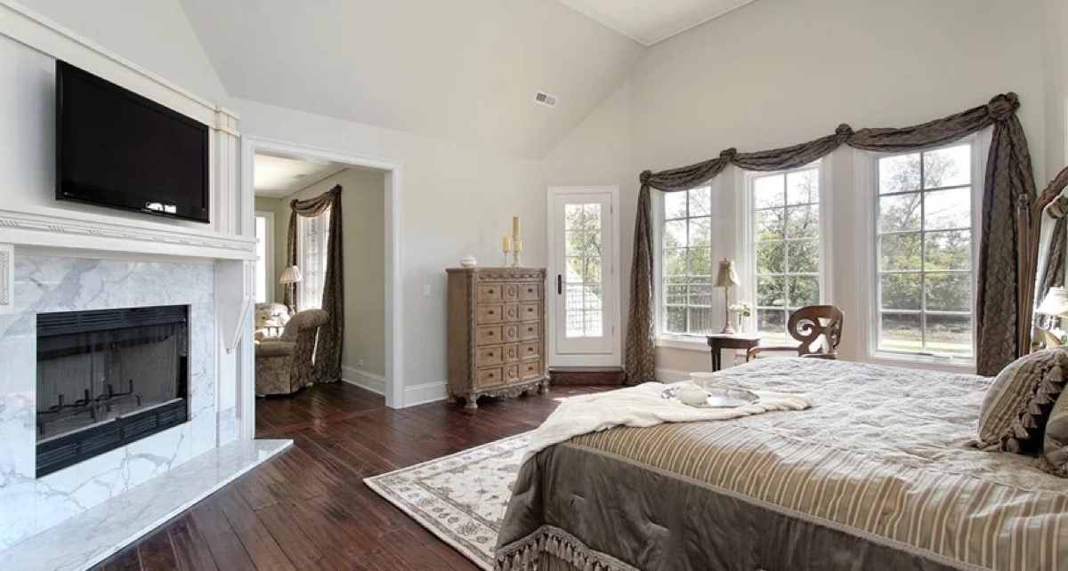 Custom master bedroom with white marble fireplace, large windows, and dark hardwood floors