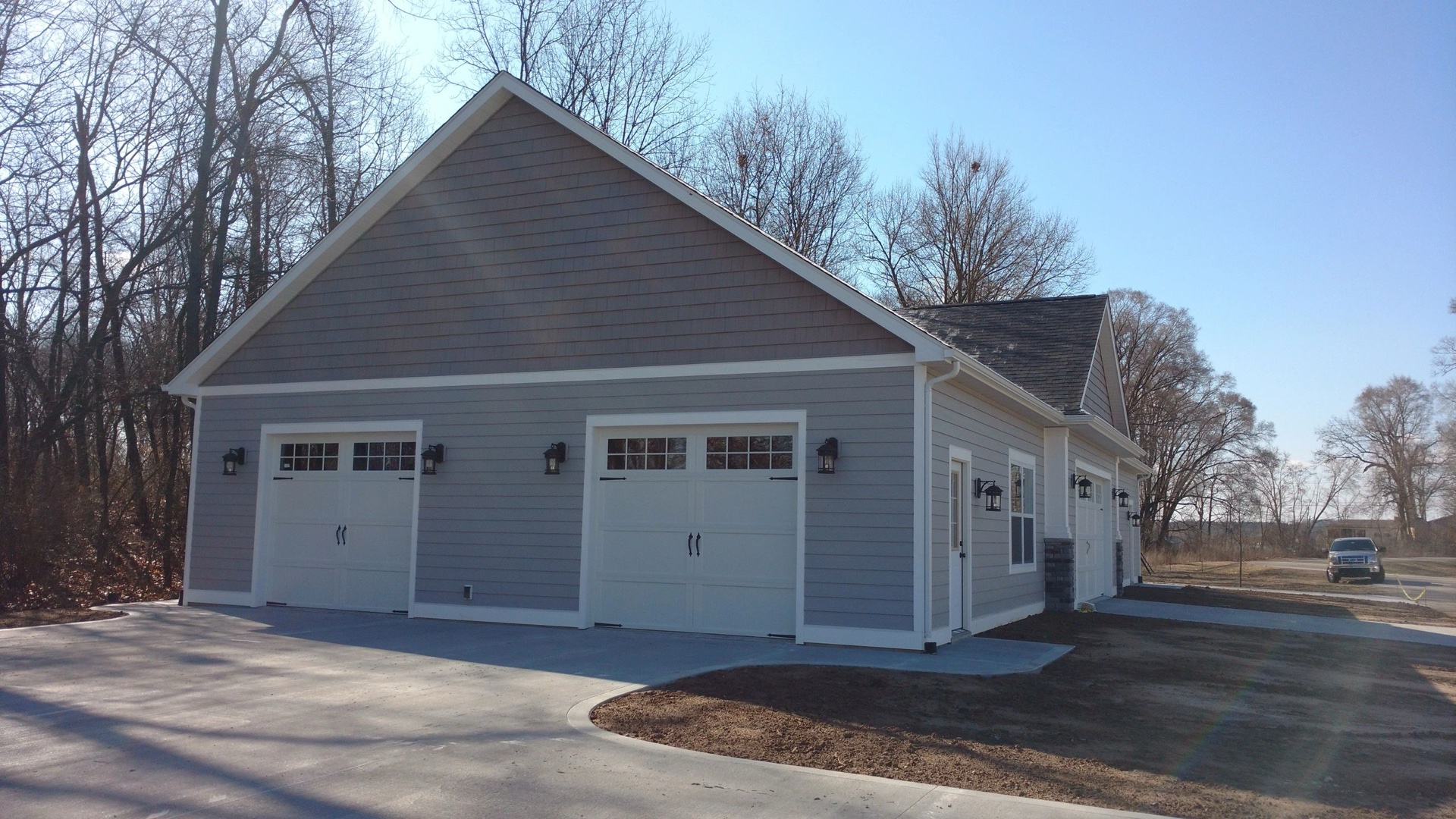 Custom three-car toy barn with carriage style overhead doors and gray craftsman siding