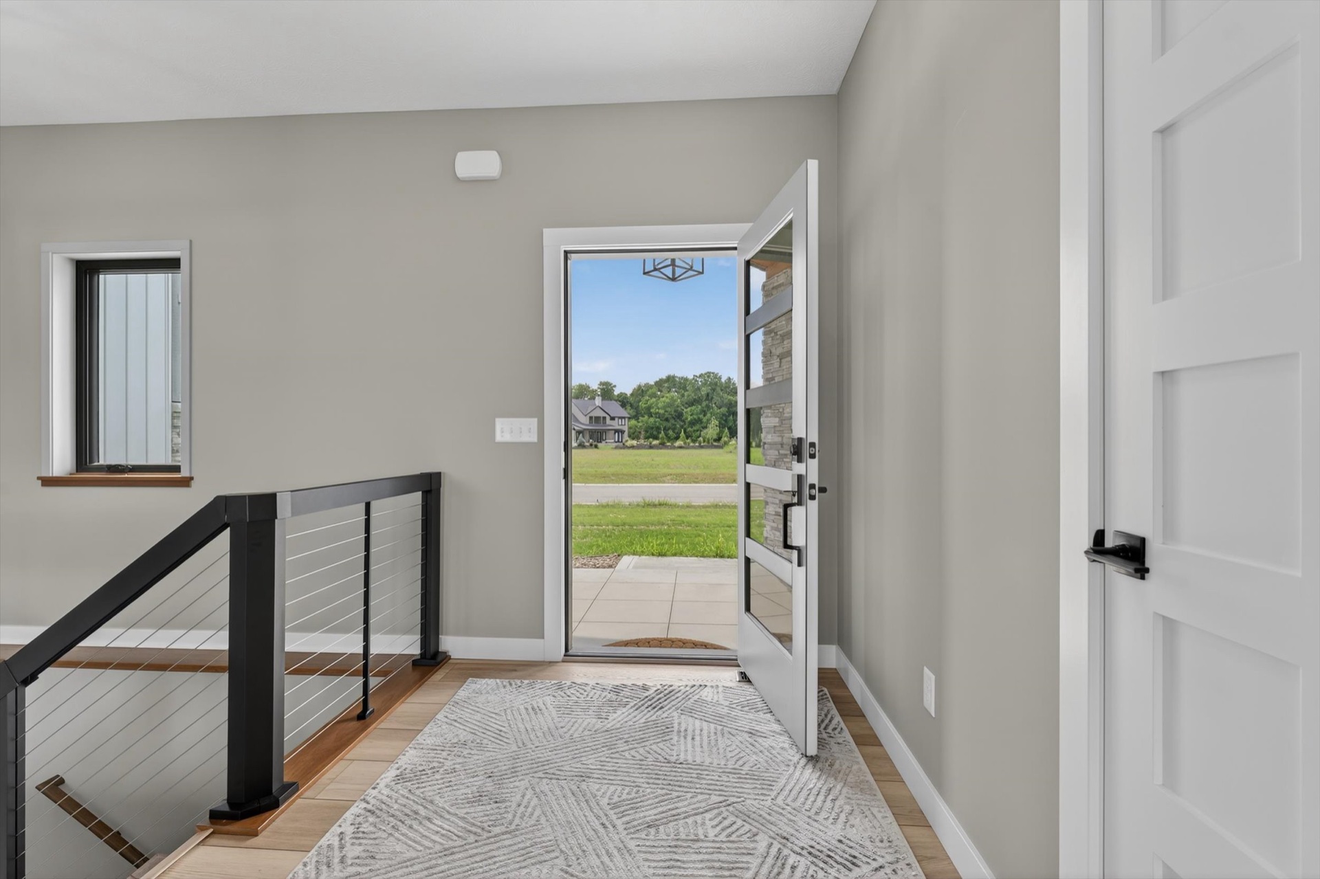 Custom home entryway with open front door, cable railing staircase, and light hardwood floors