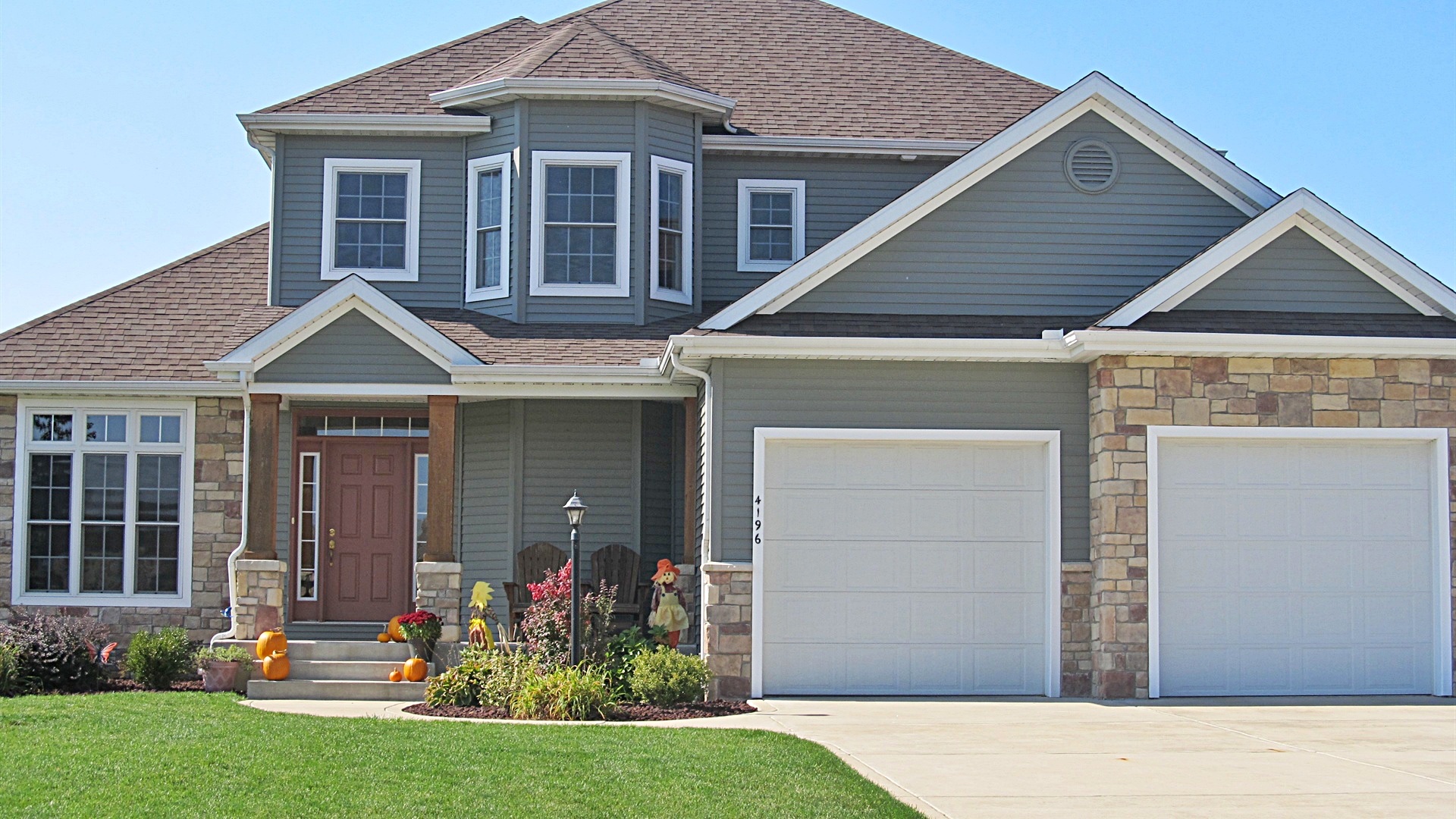 Two-story custom home with gray siding, stone base, and red front door